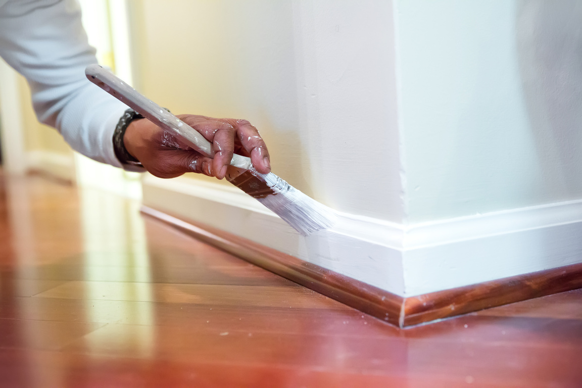 Painter paints baseboard in a home